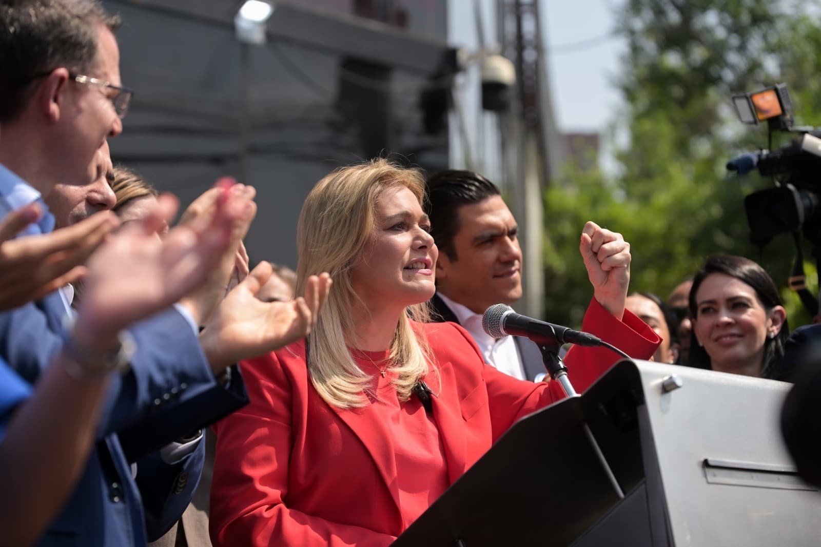 La candidata política da un discurso en un mitin, rodeada de seguidores y miembros de su equipo, mostrando entusiasmo y energía.