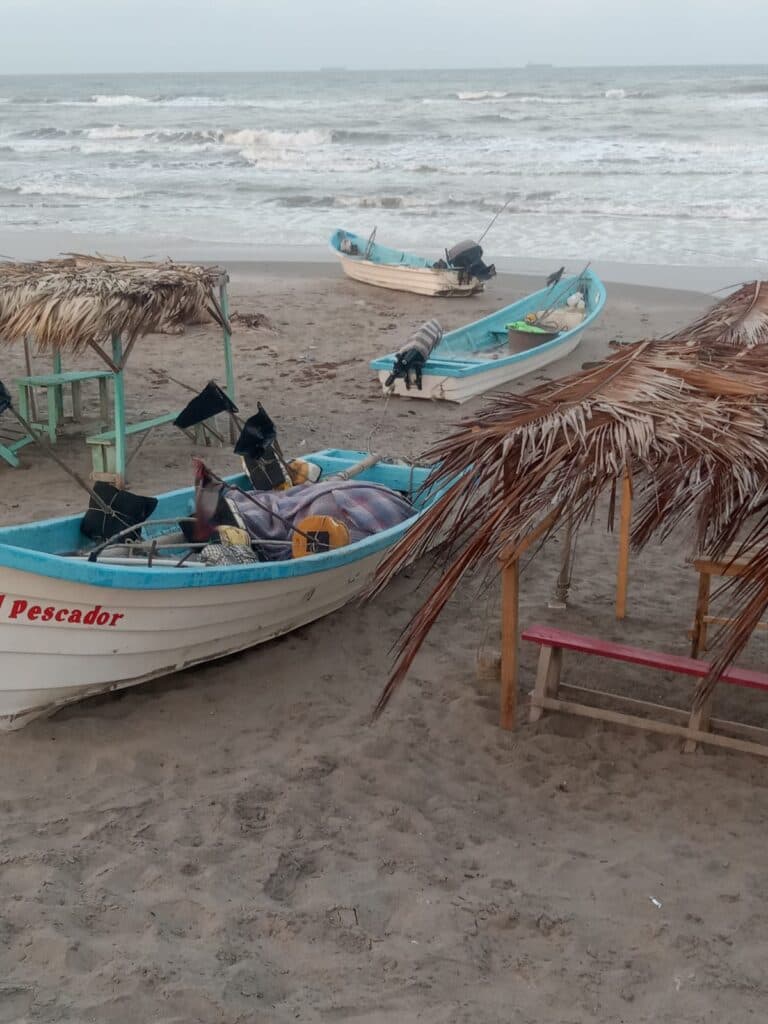 Lanchas de pescadores en la playa de Playa Hermosa, con sombrillas de palma y olas del mar al fondo, reflejando el ambiente turístico y local.