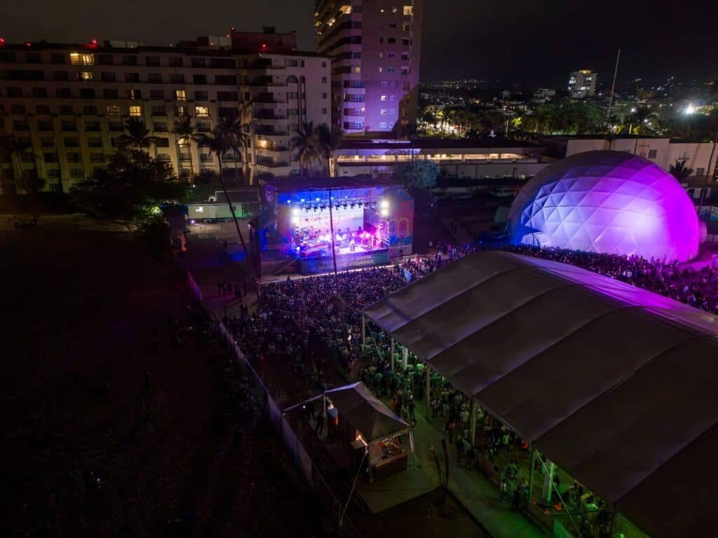 Gran concierto al aire libre en Jalisco con un público numeroso, luces coloridas y un escenario iluminado, durante el Mundial.