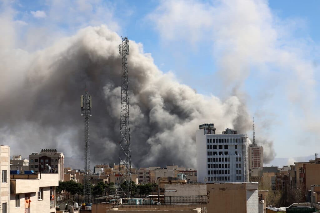 Nubes de humo oscuro se elevan sobre edificios en una ciudad, reflejando la tensión en Medio Oriente tras el anuncio de paz entre EE. UU. e Irán.