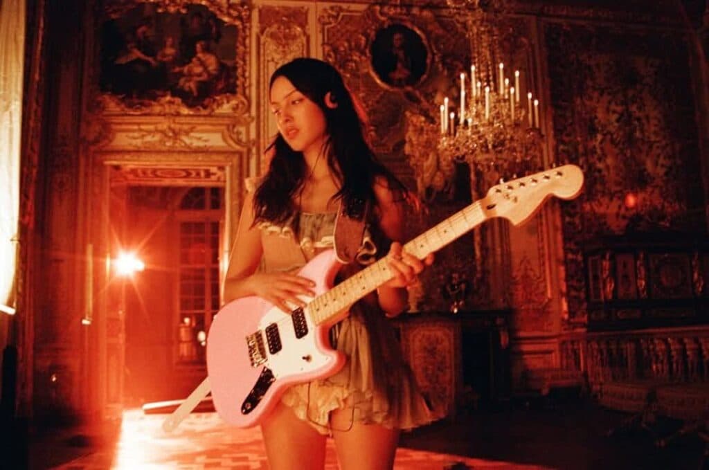 Mujer joven sosteniendo una guitarra rosa en un entorno elegante y iluminado, representando la celebración del festival