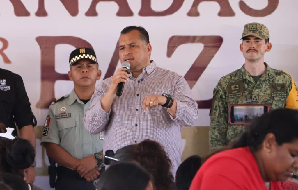 Saúl González Núñez, con micrófono en mano, habla en un evento sobre paz social, acompañado de policías y militares en Baja California Sur.