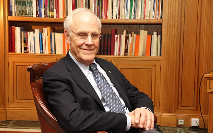 David Gross, físico y Premio Nobel, sentado en un sillón frente a una estantería con libros, reflexionando sobre el futuro de la humanidad.