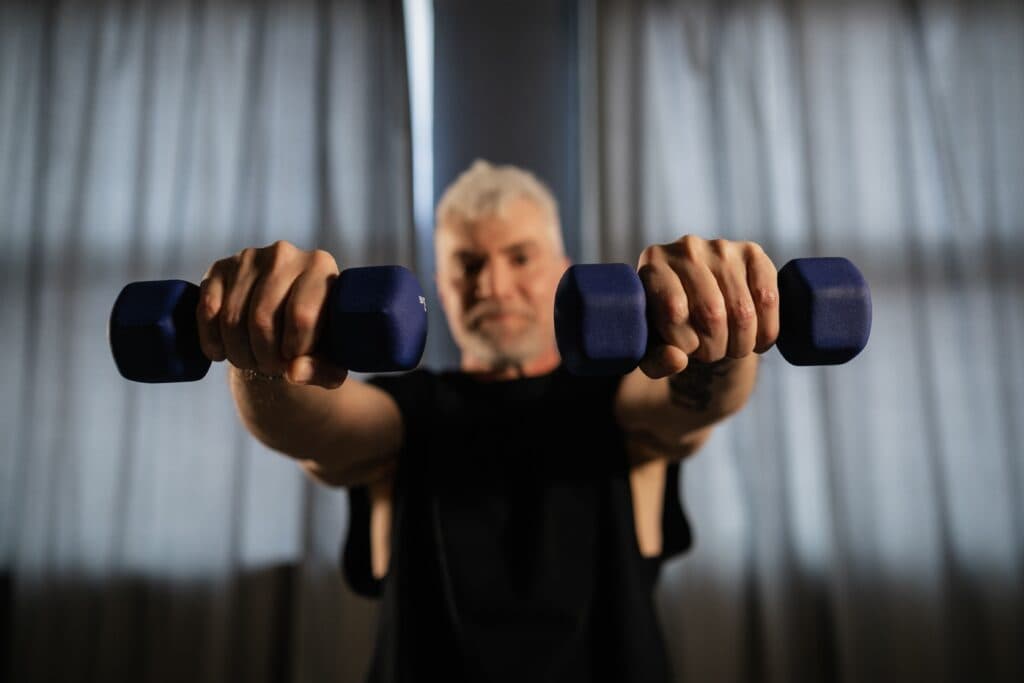 Hombre mayor sosteniendo pesas en un entorno de entrenamiento, destacando la importancia del ejercicio de fuerza para la salud en la adultez.
