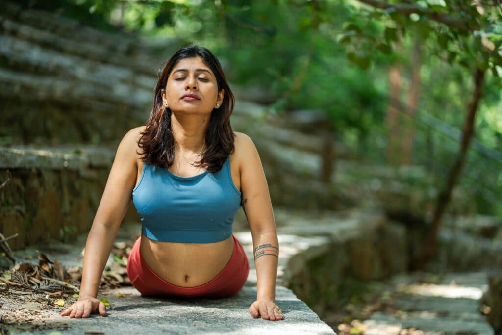 Mujer practicando yoga en un entorno natural, con enfoque en la meditación y la respiración, promoviendo el bienestar físico y mental.