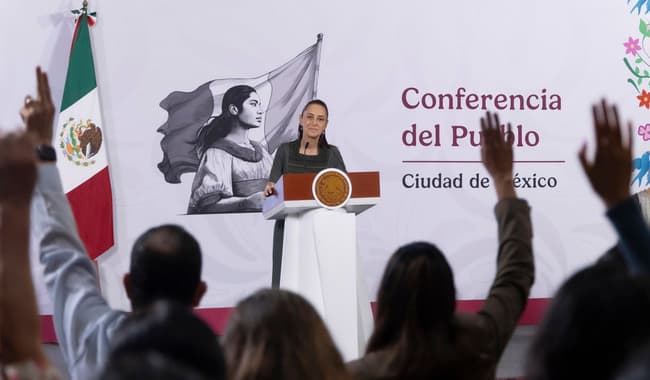 Claudia Sheinbaum Pardo durante la conferencia matutina en Palacio Nacional, con público levantando la mano en señal de participación.