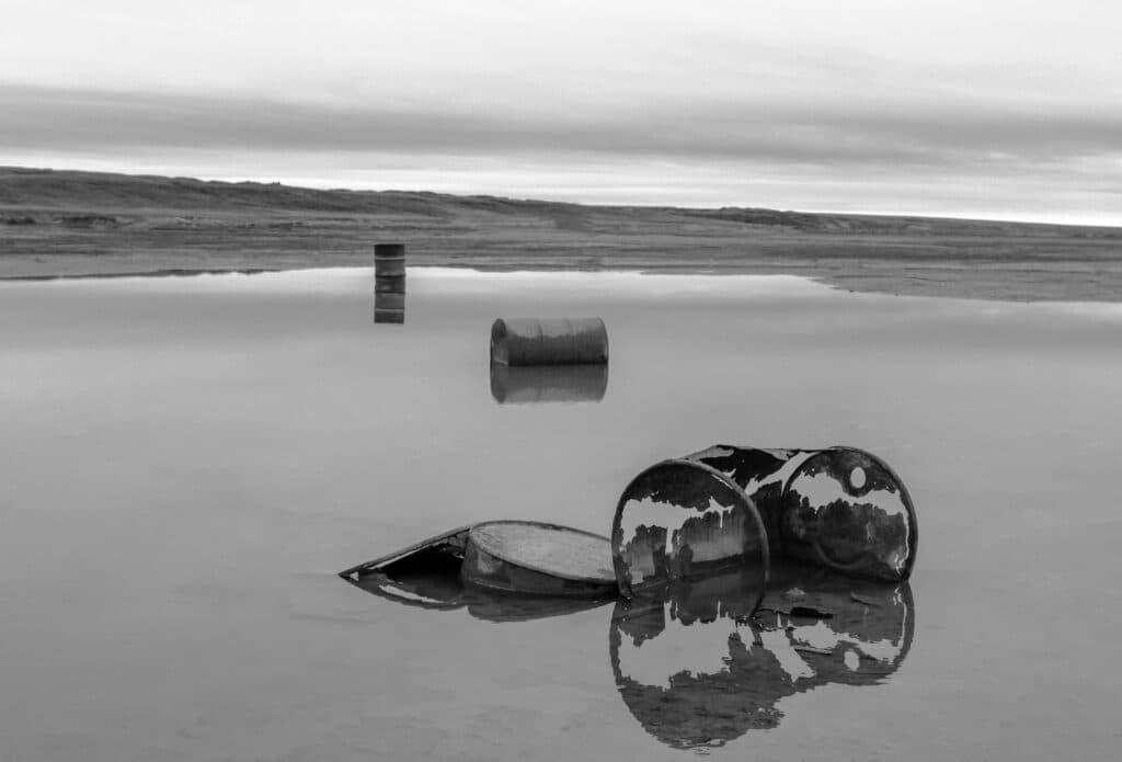 Barriles oxidados reflejados en un cuerpo de agua, simbolizando la problemática de residuos radiactivos en el océano Atlántico.