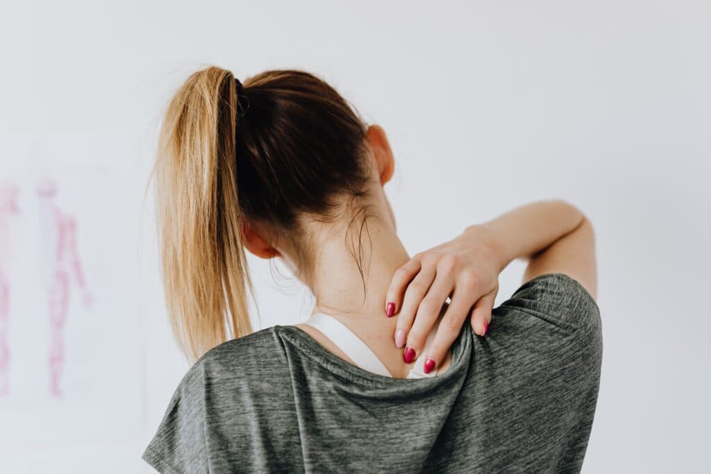 Mujer con cabello recogido se masajea el cuello, evidenciando molestias por mala postura, relacionada con la salud musculoesquelética.