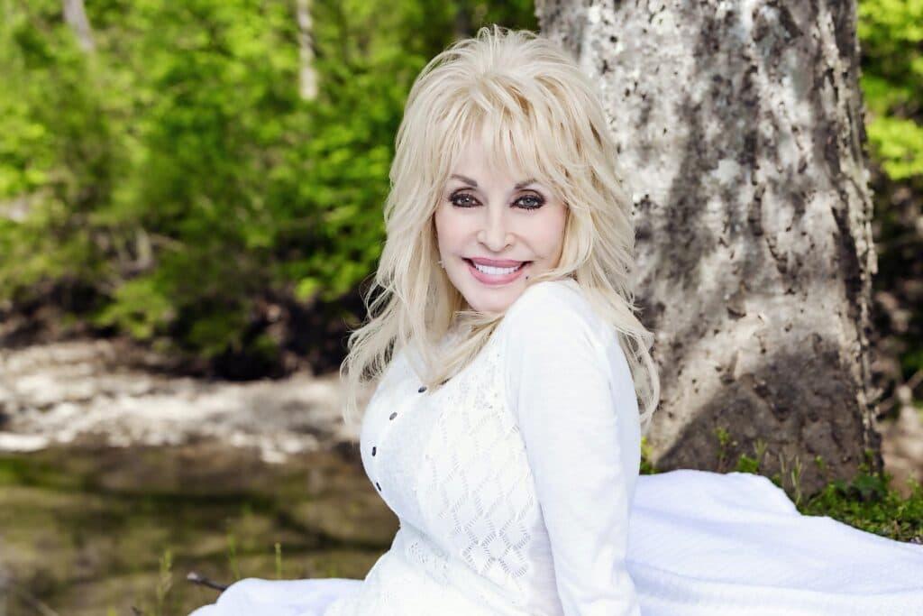 Dolly Parton sonríe en un entorno natural, recordada como una icónica figura de la música country y la cultura estadounidense.