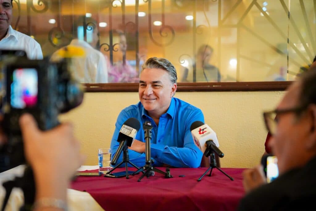 Jesús Ruiz Uribe sonríe durante una conferencia de prensa, rodeado de micrófonos y cámaras, en Mexicali, Baja California.