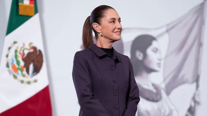 Claudia Sheinbaum durante un evento oficial, con la bandera de México de fondo, anunciando cambios en la estructura de la Presidencia.