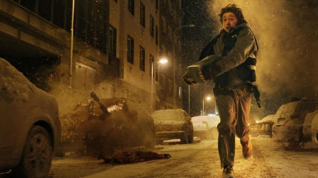 Un personaje joven corre por una calle nevada, sosteniendo un objeto, mientras explota un vehículo en el fondo, reflejando