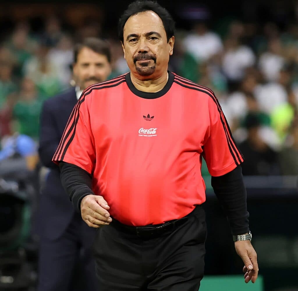Hugo Sánchez vestido con camiseta roja de árbitro, caminando en un evento deportivo, mientras se discute el VAR en la Liga MX.