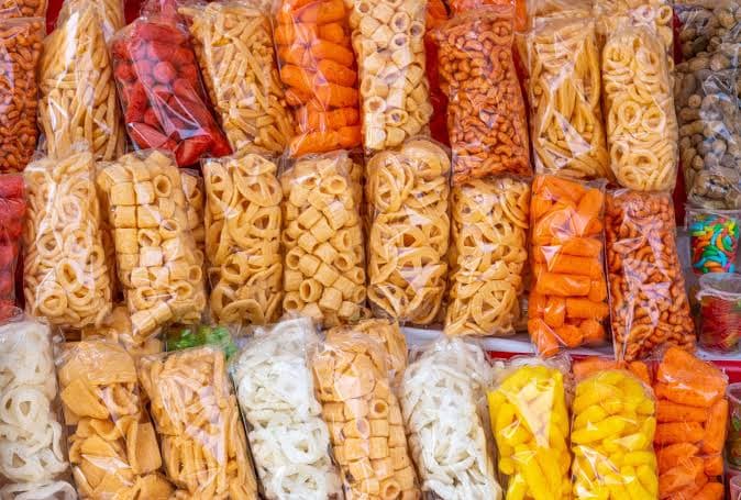 Variedad de alimentos envasados en bolsas, incluyendo botanas y dulces, reflejando la comida chatarra que se prohibirá en