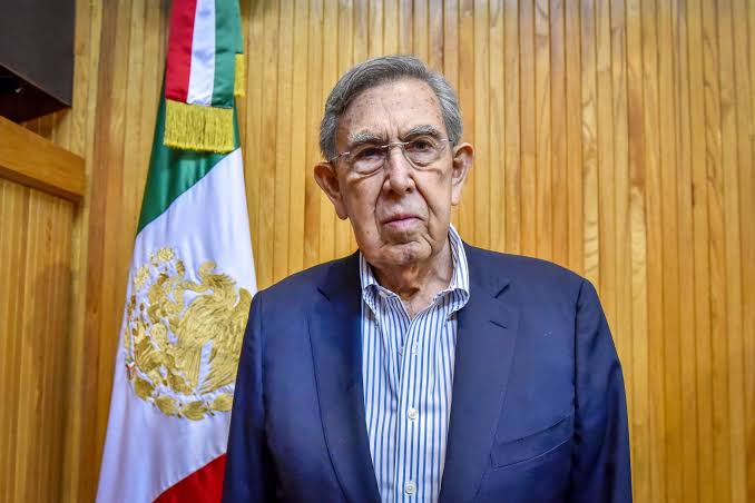 Cuauhtémoc Cárdenas, político y fundador del PRD, posa frente a la bandera de México en un evento oficial.