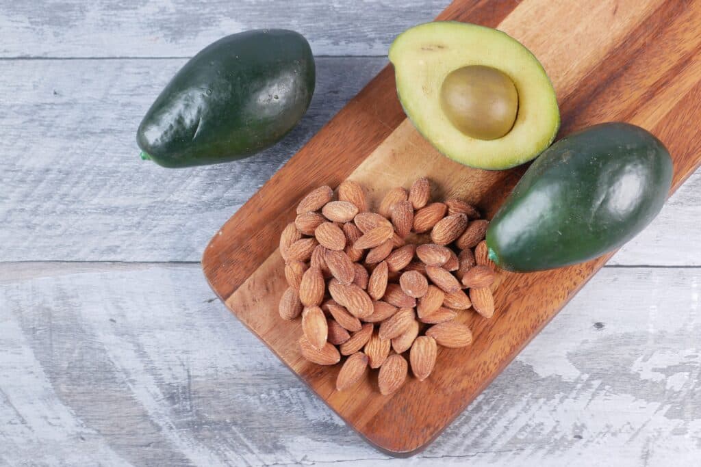 Aguacates y almendras sobre una tabla de madera, alimentos ricos en omega 3 que benefician la salud cardiovascular.